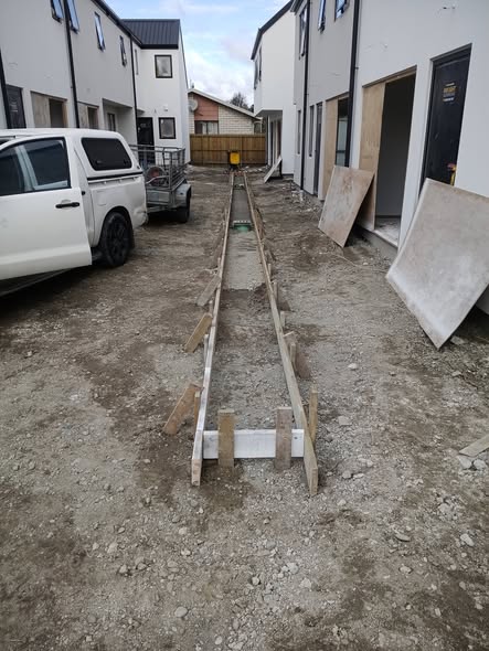 Timber-boxed drainage channel running between new townhouses with work ute and trailer on site — site preparation.