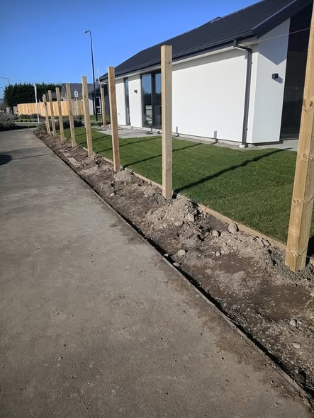 New timber fence posts set in a row along a footpath beside fresh lawn and a new home — fencing work in progress.