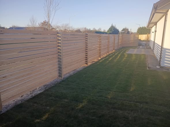 Finished horizontal-slat timber fence with lush new lawn beside a Christchurch home — fencing and landscaping by Buka Fence and Landscaping.