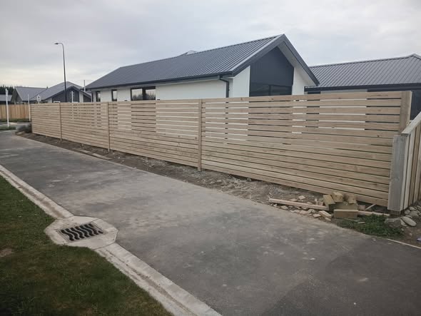 Long new horizontal-slat timber fence along a driveway with new-build homes beyond — residential fencing Christchurch.
