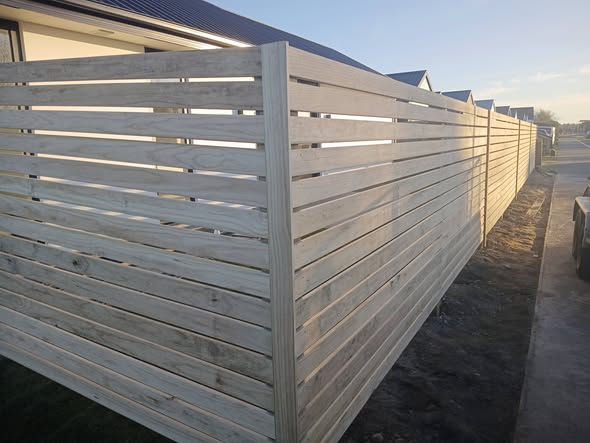 Close view of a finished horizontal-slat timber fence corner glowing in low sun — quality fence finish.