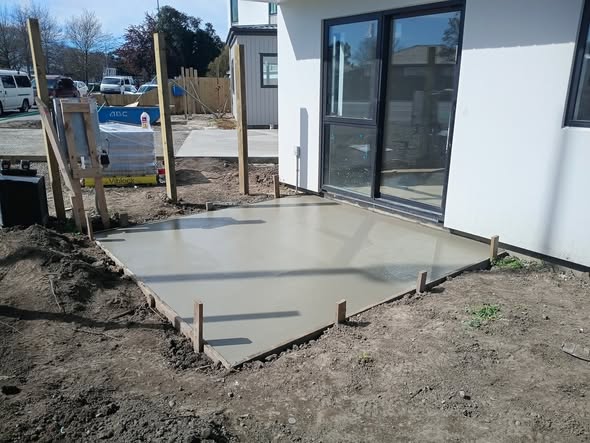Freshly poured concrete patio slab with timber boxing beside a new Christchurch home — concreting work by Buka Fence and Landscaping.