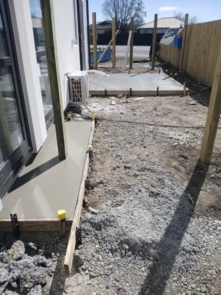 Concrete paths and patio under construction with timber boxing and yellow peg caps at a Christchurch building site.
