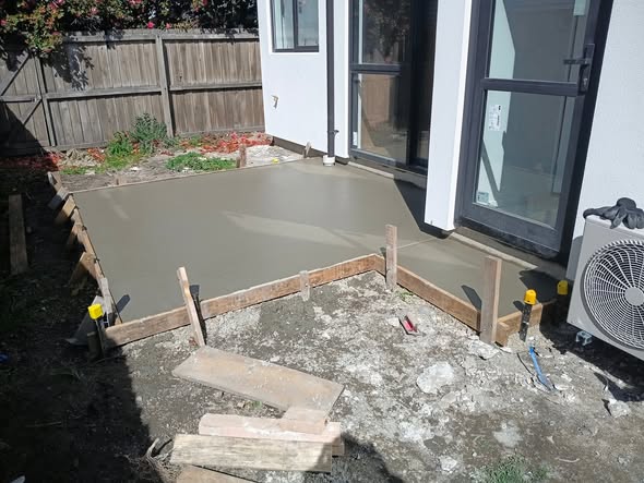 Finished smooth concrete patio with timber edging at a new Christchurch home, fenced yard beyond.