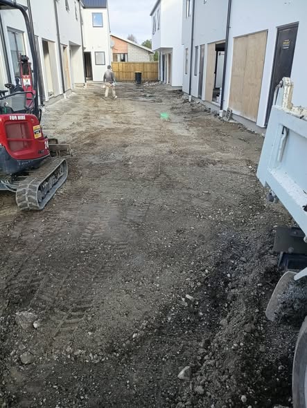 Red mini digger grading a residential site with a worker on foot and white work ute alongside — excavation in Christchurch.