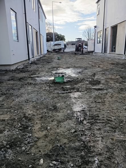 Muddy residential earthworks site with trucks and digger between new homes — excavation and site works.